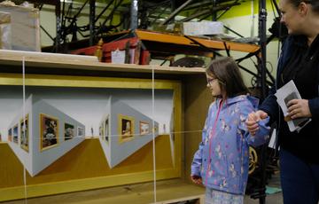 An adult and a child looking at a 3D painting stored in an open box.