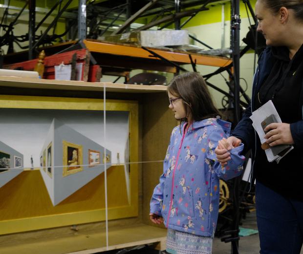 An adult and a child looking at a 3D painting stored in an open box.