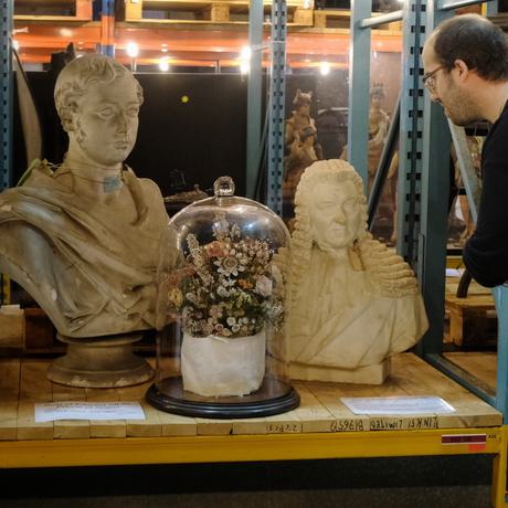 A person leaning in to take a closer look at two busts and terrarium that is on open display on warehouse shelves.