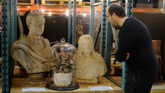 A person leaning in to take a closer look at two busts and terrarium that is on open display on warehouse shelves.