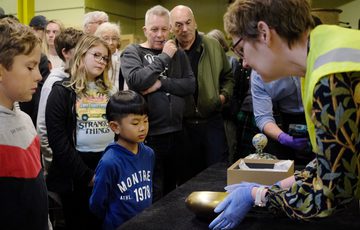 A staff member hold a gold artwork and shows it to a group of people.
