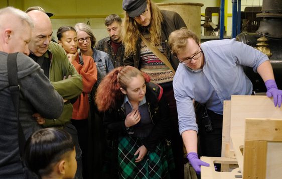 A staff member unboxes an artwork as a group of people watch.