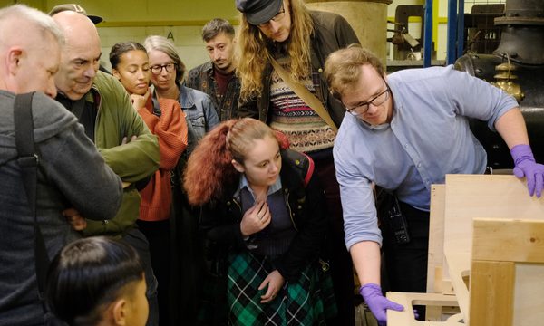 A staff member unboxes an artwork as a group of people watch.