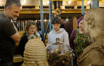 A family of two adults and two children are looking at museum objects that are on display including two sculpture and terrarium.