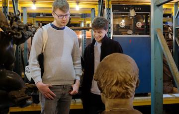 Two people looking at a bust that is on open display and stored on warehouse shelves.