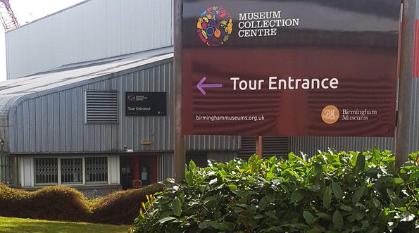 Tour entrance sign above a bush with the building and entrance behind.