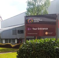 Tour entrance sign above a bush with the building and entrance behind.