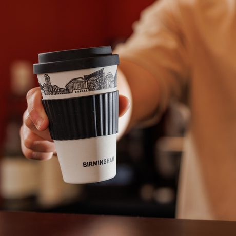 Hand holding a black and white travel coffee cup labeled "Birmingham" with city skyline.