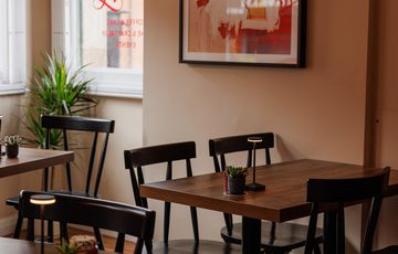 Cozy café corner with wooden tables, black chairs, small plants, and vibrant wall art.