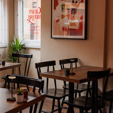 Cozy café corner with wooden tables, black chairs, small plants, and vibrant wall art.