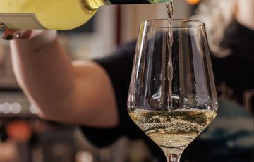 White wine is being poured from a bottle into an elegant wine glass.
