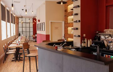 Cozy café with wooden floors, high stools, pendant lighting, and a modern coffee bar.