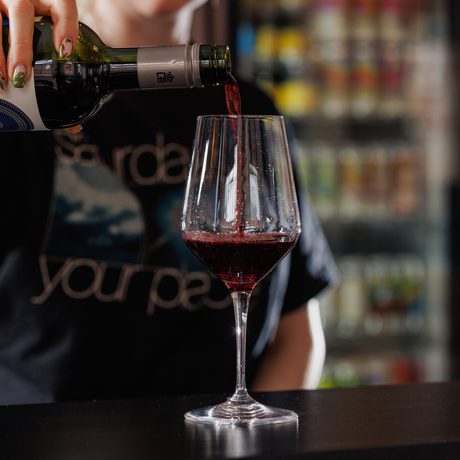 A person pours red wine from a bottle into a wine glass on a counter.