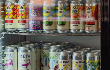 Assorted craft beer cans displayed on refrigerator shelves with colourful and varied labels.