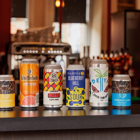Six assorted craft beer cans lined up on a bar counter with a blurred background.