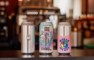 Three distinct beer cans featuring colorful, artistic designs standing on a bar counter.