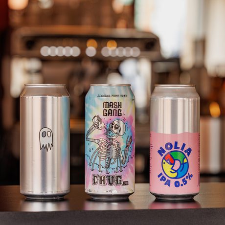 Three distinct beer cans featuring colorful, artistic designs standing on a bar counter.