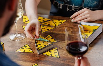 Two people playing a triangle-based card game while enjoying wine together.
