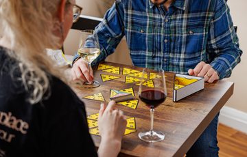 Two people enjoy wine while playing a triangular game at a wooden table.