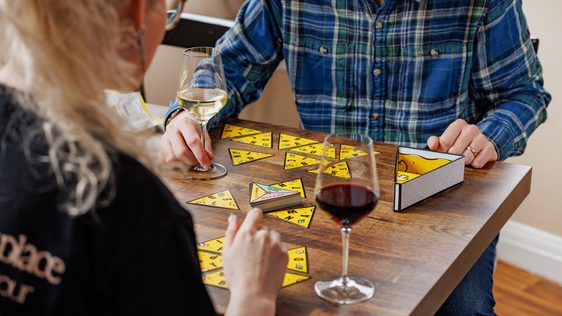 Two people enjoy wine while playing a triangular game at a wooden table.