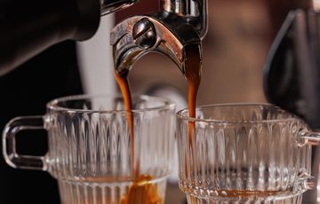 Espresso machine extracts coffee into two clear glass cups simultaneously.