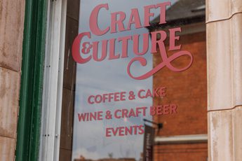A green window with sign that read 'Craft & Culture coffee, cake, wine, craft beer, and events'.