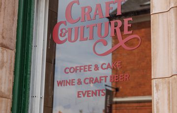 A green window with sign that read 'Craft & Culture coffee, cake, wine, craft beer, and events'.