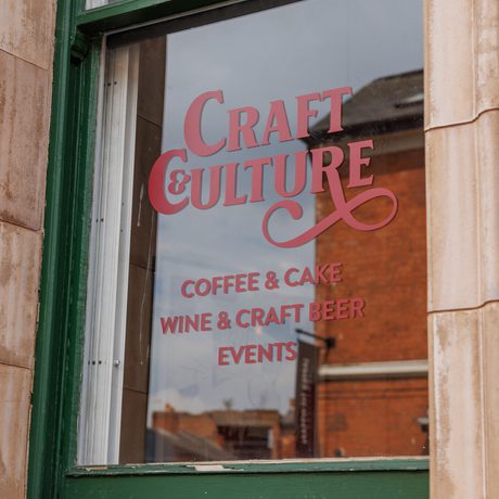 A green window with sign that read 'Craft & Culture coffee, cake, wine, craft beer, and events'.