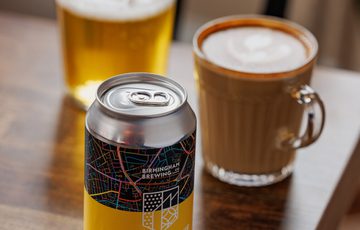 Craft beer can on wooden table with a glass of beer and latte.
