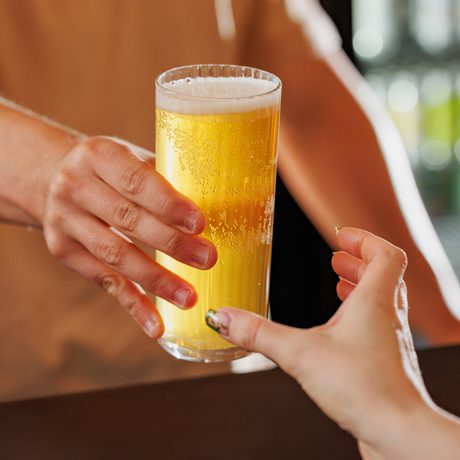 One person hands a cold beer with foam to another across a counter.