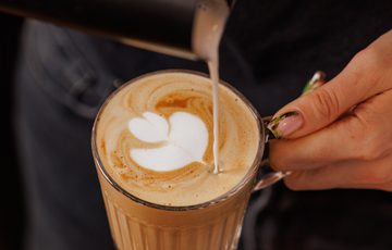 Barista pouring milk to create latte art on a cup of coffee.