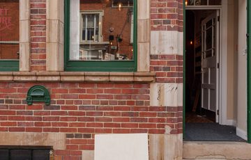 Brick building front with green window, partially open green door, and a Craft & Culture sign outside.