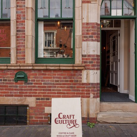 Brick building front with green window, partially open green door, and a Craft & Culture sign outside.