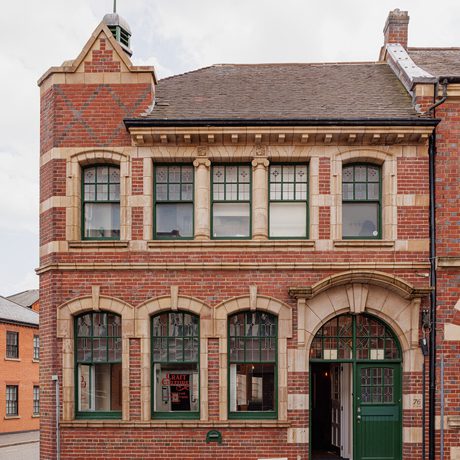 Two-story brick building with arched doorway, green doors and multiple windows.