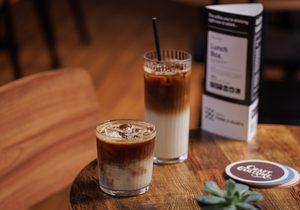 Two iced drinks, a menu, coaster, and a small succulent on a wooden table.