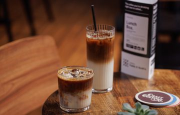 Two iced drinks, a menu, coaster, and a small succulent on a wooden table.