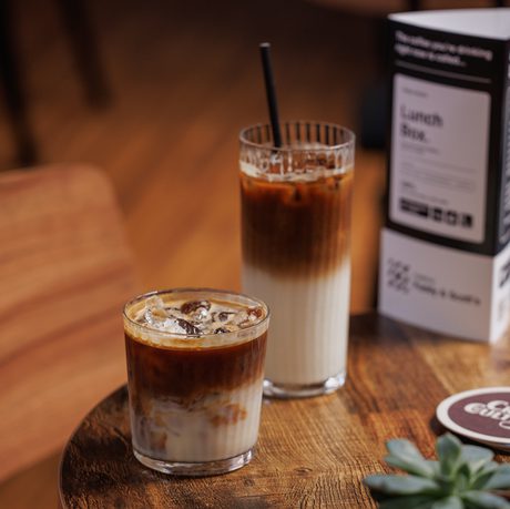 Two iced drinks, a menu, coaster, and a small succulent on a wooden table.