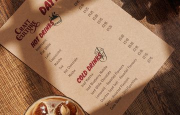 Daytime cold and hot drink menu with iced beverages on a wooden table beside a succulent plant.