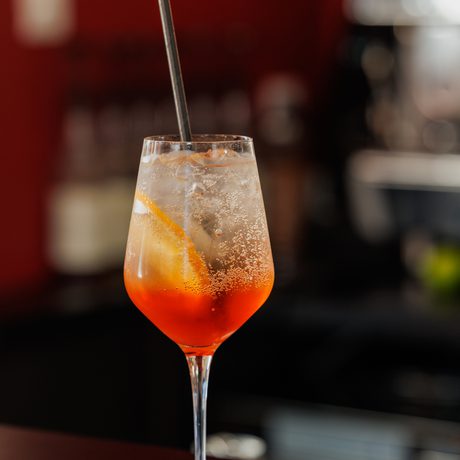 A refreshing orange cocktail with ice and a straw in a wine glass on a dark worktop.