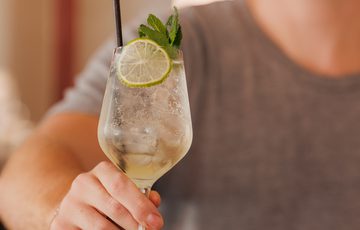 A man holding a refreshing cocktail garnished with lime and mint leaves.
