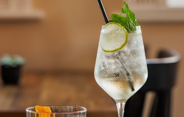 Two refreshing cocktails, one red with an orange twist, one clear with lime and mint.