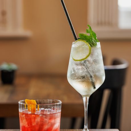 Two refreshing cocktails, one red with an orange twist, one clear with lime and mint.