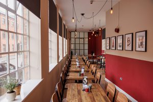 Cozy café with wooden tables, large windows, pendant lights, and framed artwork on red wall.