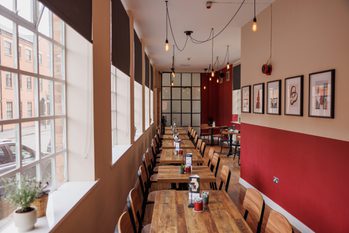 Cozy café with wooden tables, large windows, pendant lights, and framed artwork on red wall.