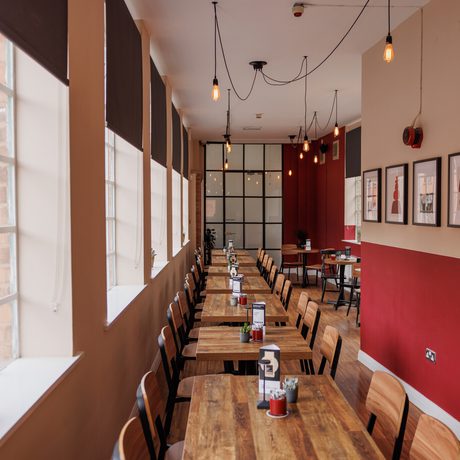 Cozy café with wooden tables, large windows, pendant lights, and framed artwork on red wall.