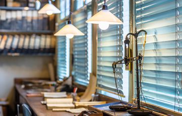 Vintage office with wooden desk, typewriter, stacks of paper, and hanging pendant lights.