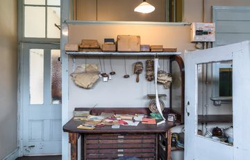Vintage workspace with papers, measuring instruments, hanging tools, and storage cabinet in a well-lit room.