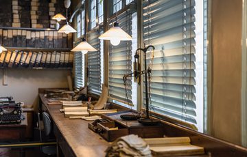 Vintage office with wooden desk, typewriter, stacks of paper, and hanging pendant lights.