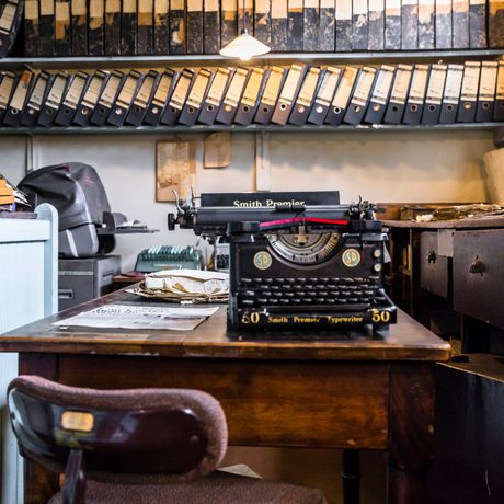 Vintage typewriter on wooden desk surrounded by filing cabinets and binders in office.