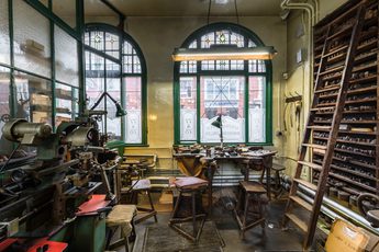 Workshop with machinery, a workbench in front of a window and wooden shelves with a ladder